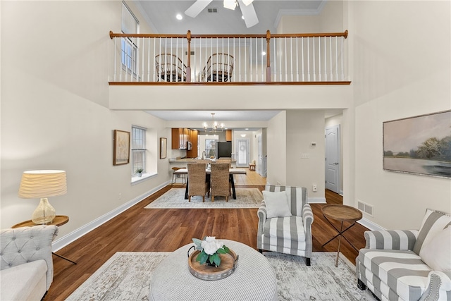 living area featuring a high ceiling, visible vents, baseboards, and wood finished floors