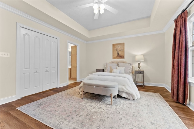 bedroom featuring ceiling fan, wood finished floors, baseboards, a closet, and a raised ceiling