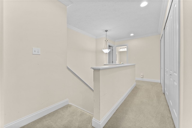 hallway with ornamental molding, baseboards, light carpet, and an upstairs landing