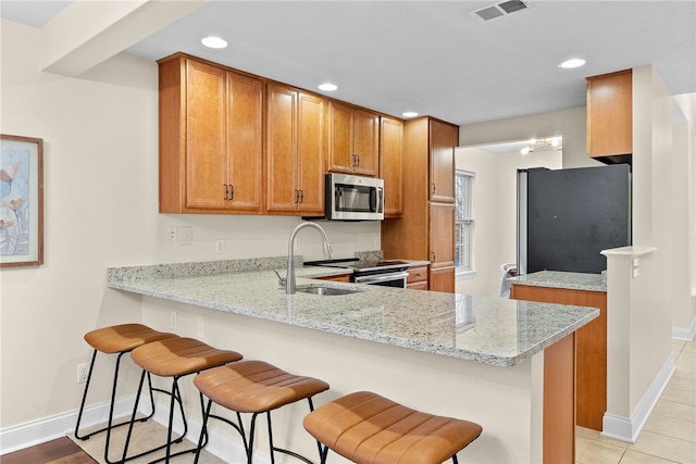 kitchen featuring light stone counters, a peninsula, visible vents, appliances with stainless steel finishes, and brown cabinets