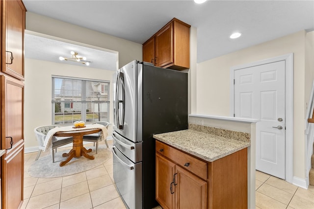 kitchen featuring light tile patterned floors, baseboards, brown cabinetry, freestanding refrigerator, and light stone countertops