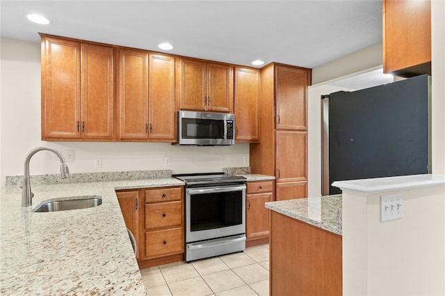 kitchen with light tile patterned floors, light stone countertops, stainless steel appliances, a sink, and brown cabinets