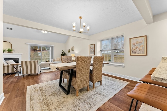 dining space with vaulted ceiling with beams, a notable chandelier, a fireplace, visible vents, and dark wood finished floors