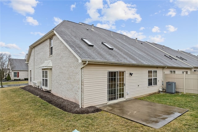 rear view of house featuring brick siding, a patio, a lawn, central AC, and fence