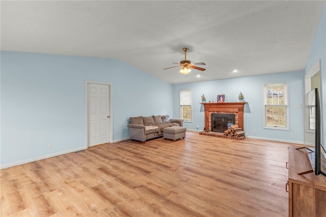 living area featuring lofted ceiling, light wood-type flooring, a fireplace, and baseboards