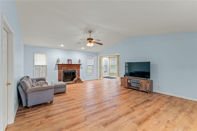 living area with ceiling fan, baseboards, vaulted ceiling, light wood-style floors, and a brick fireplace