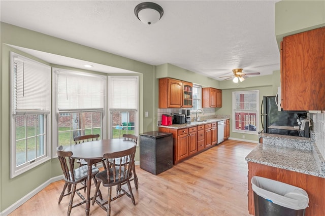 kitchen featuring electric stove, tasteful backsplash, brown cabinetry, white dishwasher, and a sink