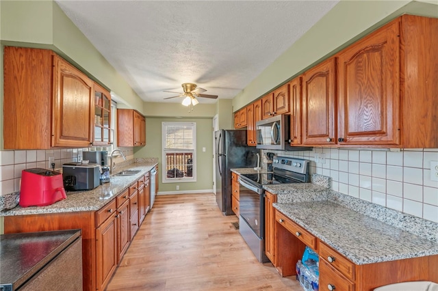 kitchen with light wood-type flooring, appliances with stainless steel finishes, brown cabinetry, and a sink