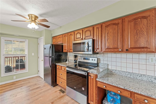 kitchen with stainless steel appliances, decorative backsplash, brown cabinetry, light stone countertops, and light wood-type flooring