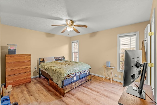 bedroom featuring baseboards, ceiling fan, a textured ceiling, and light wood finished floors