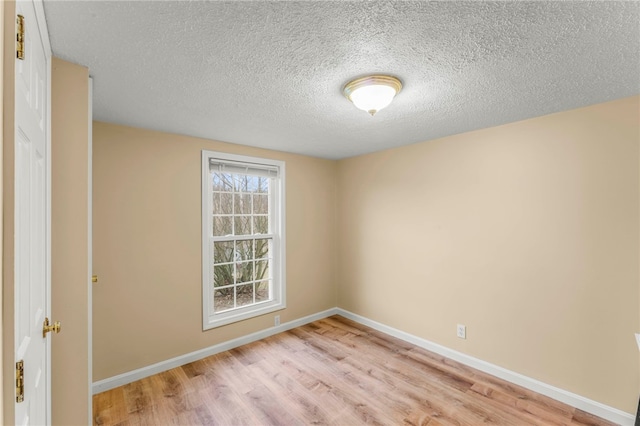 empty room featuring light wood-style flooring, baseboards, and a textured ceiling