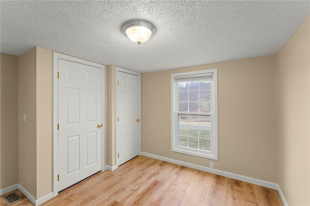 unfurnished bedroom featuring baseboards, a textured ceiling, visible vents, and light wood-style floors