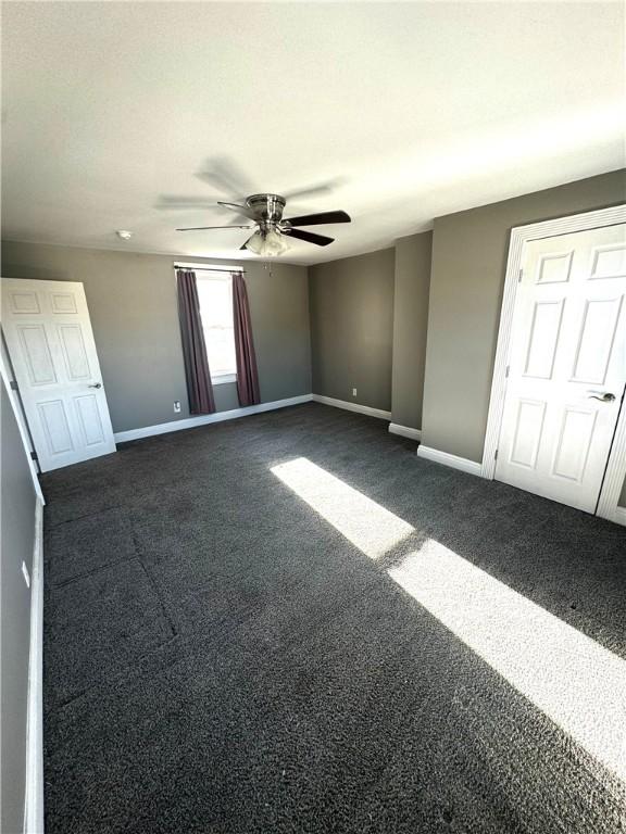 unfurnished bedroom with dark carpet, baseboards, and ceiling fan