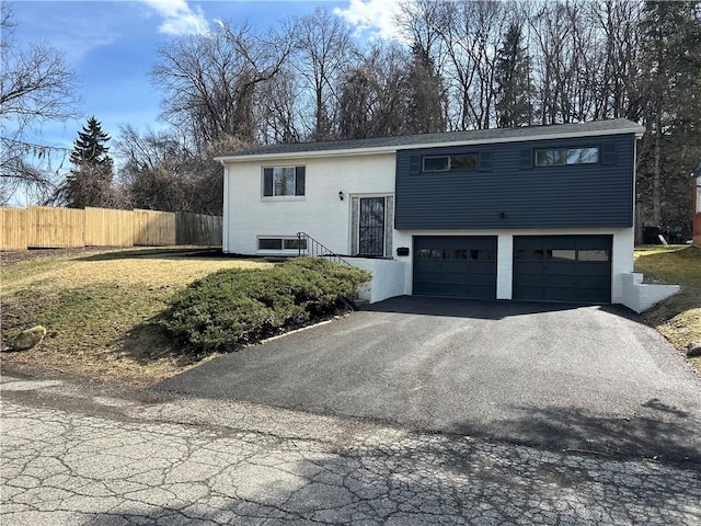 bi-level home with an attached garage, fence, and aphalt driveway