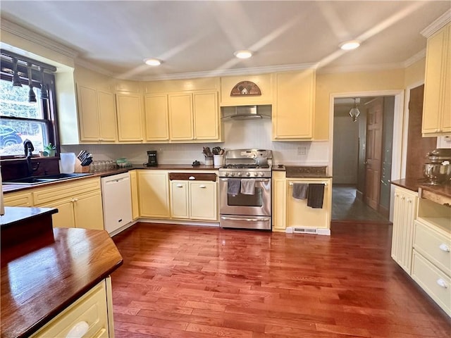 kitchen featuring stainless steel gas range oven, wall chimney exhaust hood, dark wood-style flooring, cream cabinets, and white dishwasher