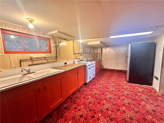 kitchen featuring wooden walls, freestanding refrigerator, dark colored carpet, and white gas range oven