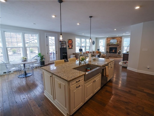 kitchen with dark wood finished floors, a sink, open floor plan, dishwasher, and cream cabinetry