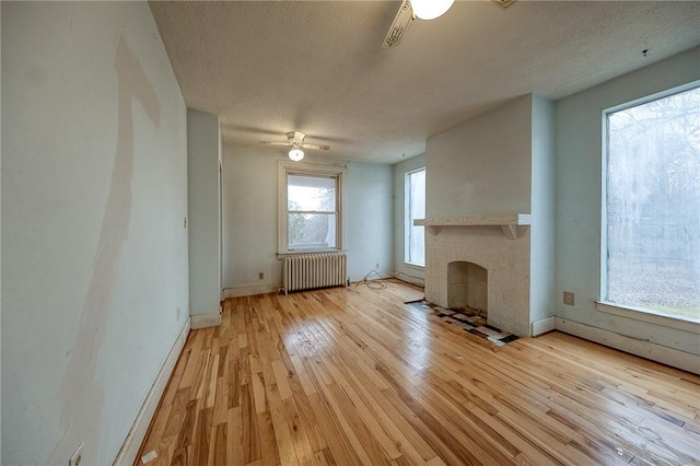 unfurnished living room with ceiling fan, baseboards, light wood-style floors, a brick fireplace, and radiator heating unit