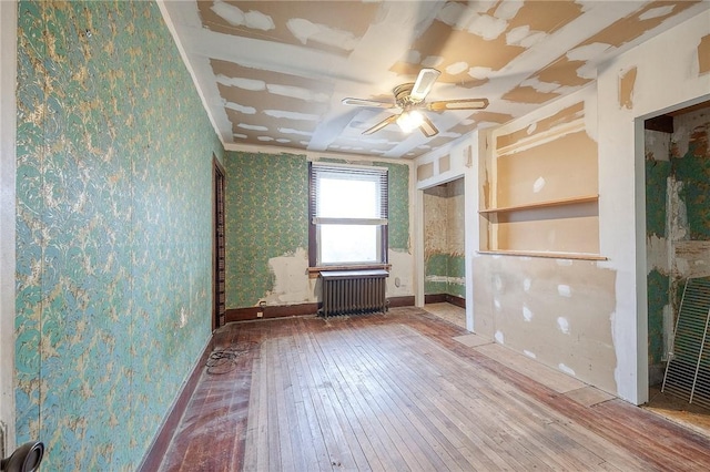 spare room with radiator, hardwood / wood-style floors, a ceiling fan, baseboards, and wallpapered walls