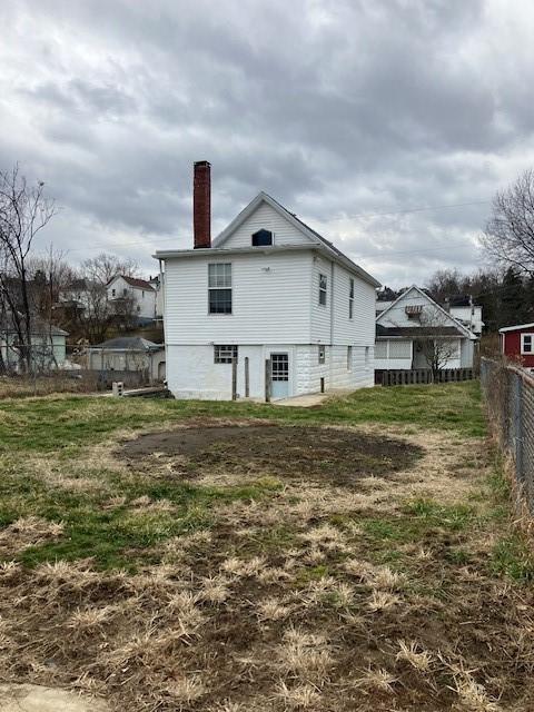 rear view of property featuring a chimney and fence