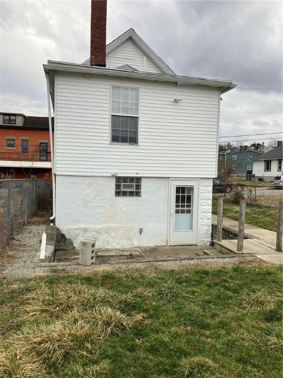 rear view of house with a chimney, fence, and a lawn