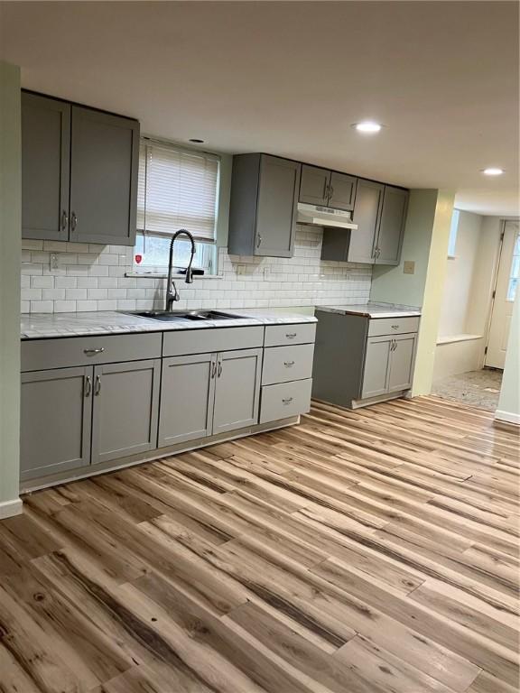 kitchen featuring tasteful backsplash, gray cabinets, a sink, light wood-type flooring, and under cabinet range hood