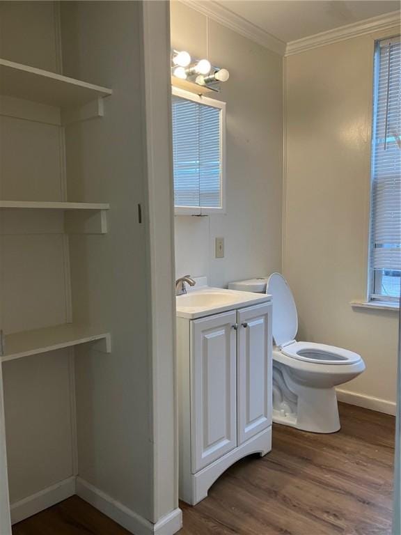 half bathroom featuring toilet, wood finished floors, vanity, baseboards, and crown molding