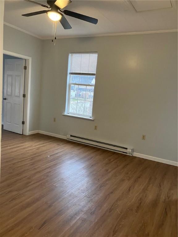 empty room featuring crown molding, baseboard heating, dark wood-type flooring, a ceiling fan, and baseboards