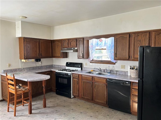 kitchen with tasteful backsplash, under cabinet range hood, light countertops, black appliances, and a sink