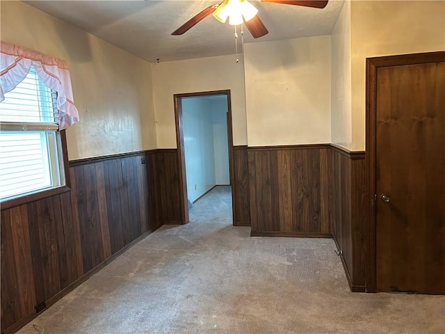 empty room featuring a wainscoted wall, wooden walls, a ceiling fan, and carpet flooring