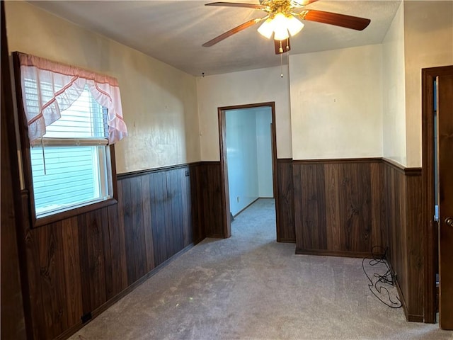 spare room with a ceiling fan, carpet, a wainscoted wall, and wooden walls