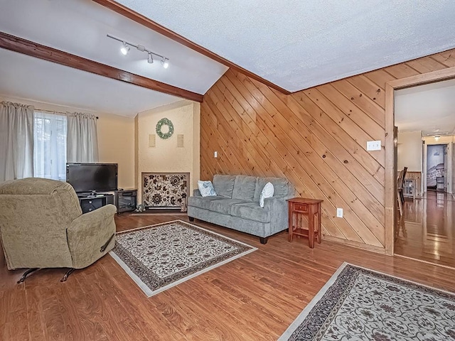 living room featuring a textured ceiling, wooden walls, beam ceiling, and wood finished floors