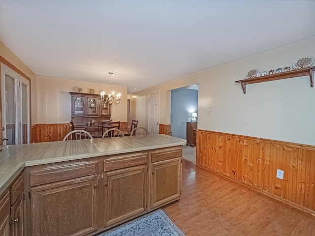 kitchen with a chandelier, wood walls, light wood-style floors, light countertops, and wainscoting