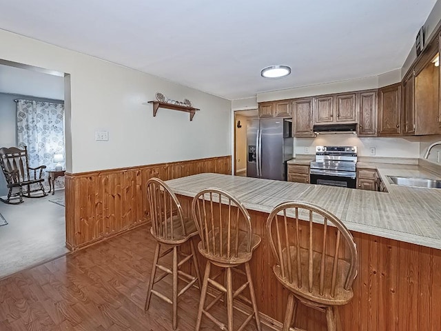 kitchen with a wainscoted wall, appliances with stainless steel finishes, range hood, light countertops, and a sink