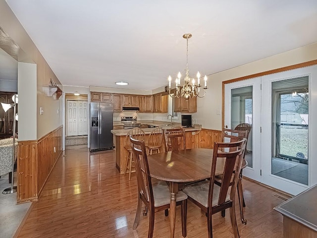 dining space with wooden walls, a notable chandelier, wood finished floors, visible vents, and wainscoting