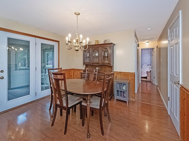 dining space with a wainscoted wall, wood walls, a chandelier, and light wood-style floors