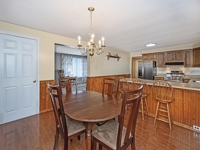 dining room featuring wood walls, wainscoting, dark wood finished floors, and a notable chandelier