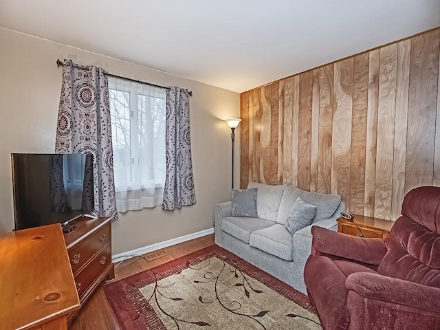 living room featuring wood walls, baseboards, and wood finished floors