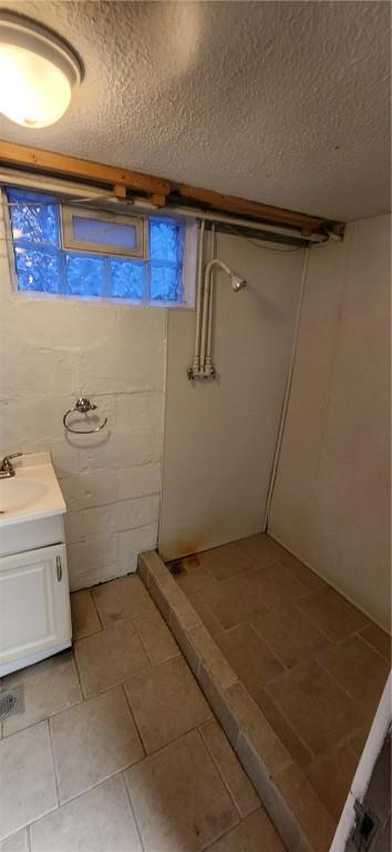 full bath with a textured ceiling, tile patterned flooring, walk in shower, and vanity