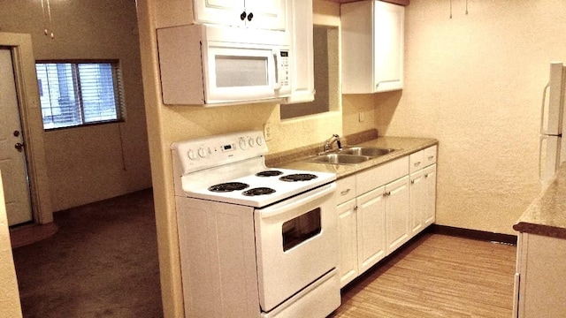 kitchen featuring white appliances, wood finished floors, a sink, white cabinets, and light countertops