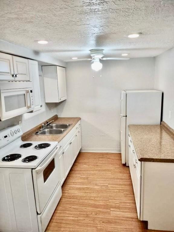 kitchen with light wood finished floors, white cabinets, a sink, a textured ceiling, and white appliances