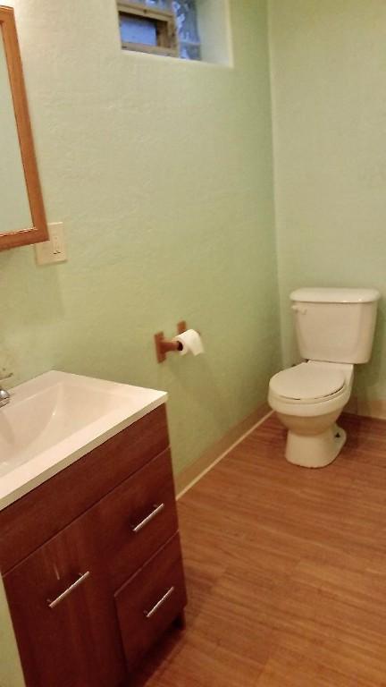 half bathroom with toilet, baseboards, wood finished floors, and vanity