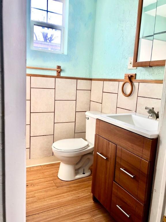 half bath featuring wainscoting, toilet, wood finished floors, vanity, and tile walls