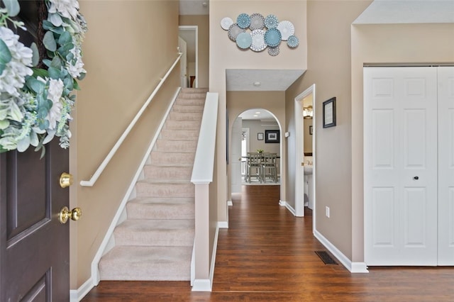 foyer entrance with arched walkways, wood finished floors, visible vents, baseboards, and stairway