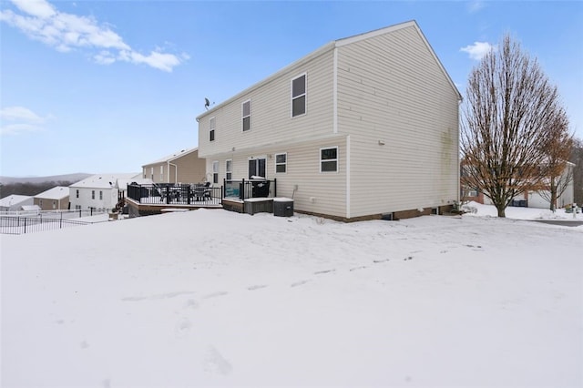 snow covered rear of property featuring fence, a deck, and cooling unit