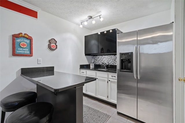 kitchen with a breakfast bar area, a peninsula, a sink, stainless steel refrigerator with ice dispenser, and decorative backsplash