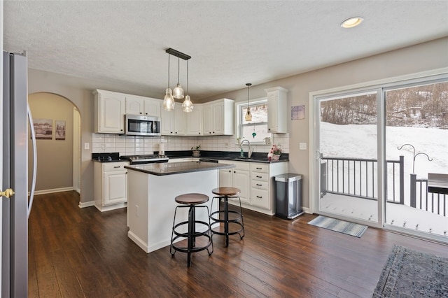 kitchen featuring arched walkways, stainless steel appliances, dark countertops, and white cabinetry