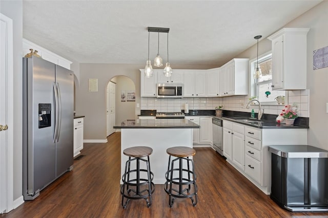 kitchen featuring arched walkways, dark countertops, appliances with stainless steel finishes, white cabinets, and a sink