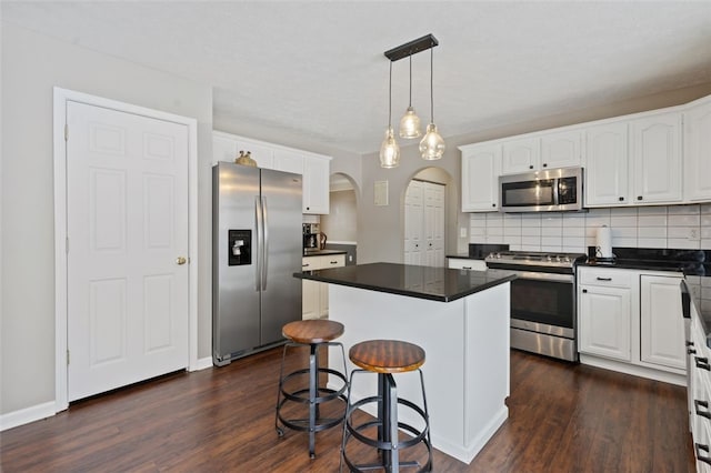 kitchen with arched walkways, dark wood-style flooring, a center island, stainless steel appliances, and decorative backsplash