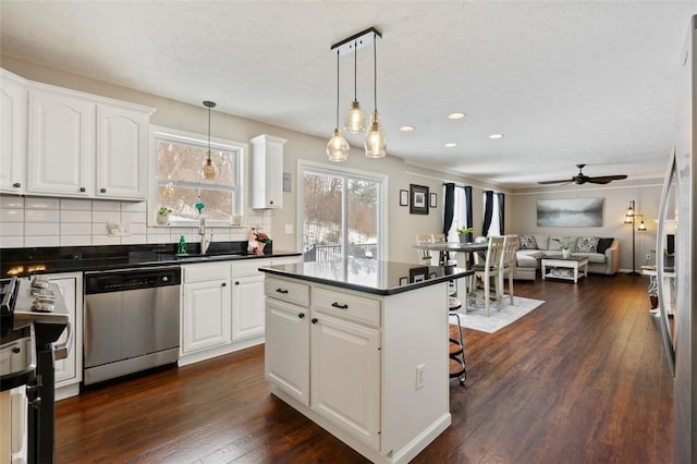 kitchen with dark wood-style flooring, dark countertops, a sink, dishwasher, and a kitchen breakfast bar